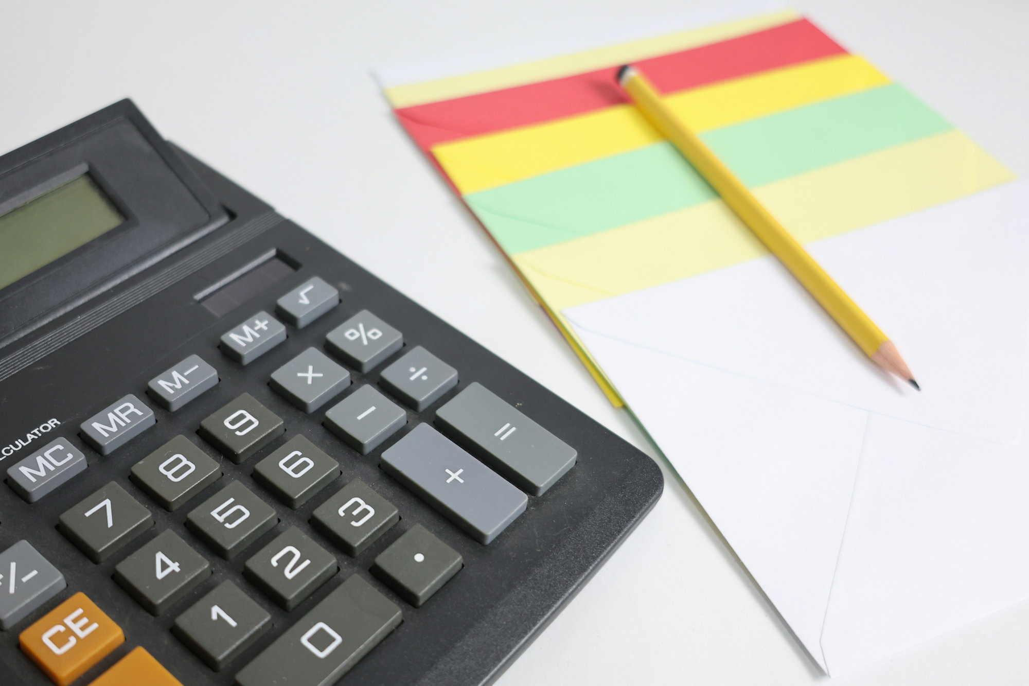 Calculator and notepad with pencil on white surface